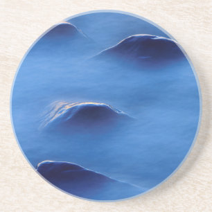 Sunset on rocks protruding through foamy water coaster