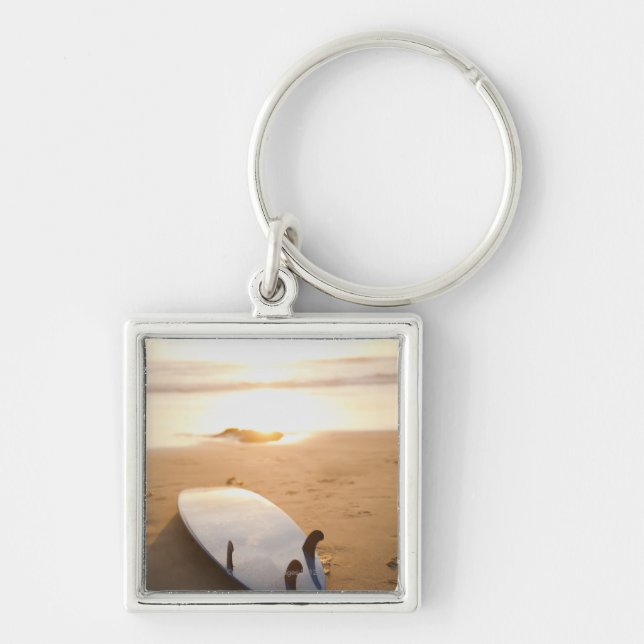 Surfboard laying on beach at sunset keychain (Front)
