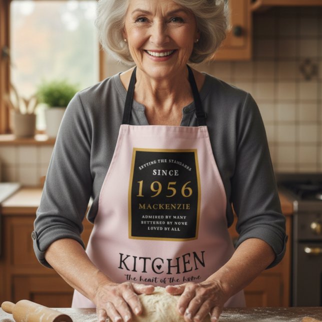 Tablier 70e anniversaire 1952 Nom Elégant Black Gold Rose (1956 pink apron worn by a woman in a kitchen baking)