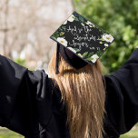 The Adventure Begins | Custom Class Year Graduation Cap Topper<br><div class="desc">Beautiful grad cap topper features the quote "And so the adventure begins" in white script lettering on a black background adorned with white watercolor flowers and green foliage. Personalize with your class year and/or school.</div>