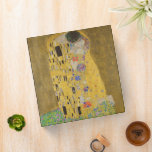 The Lovers Kissing Embrace by Gustav Klimt Binder<br><div class="desc">Sunlight glints off the swirling golden embrace that surrounds the lovers in Gustav Klimt's masterpiece, The Kiss. The scene is a paradox of intimacy and isolation. The couple stands on a precipice, a field of colourful flowers at their feet, yet they are oblivious to the world around them. Their gazes...</div>