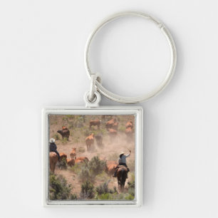 Three cowboys and cowgirls driving cattle keychain