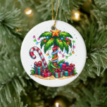 Tropical Christmas Palm Tree Ceramic Ornament<br><div class="desc">An ornament with a seasonal holiday image. A tropical palm tree decorated in festive lights with a star on top. A giant red and white candy cane sticking out of the sand. Christmas presents under the tree. Whimsical and fun.</div>