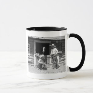 Two cowboys standing next to a barn with a horse mug