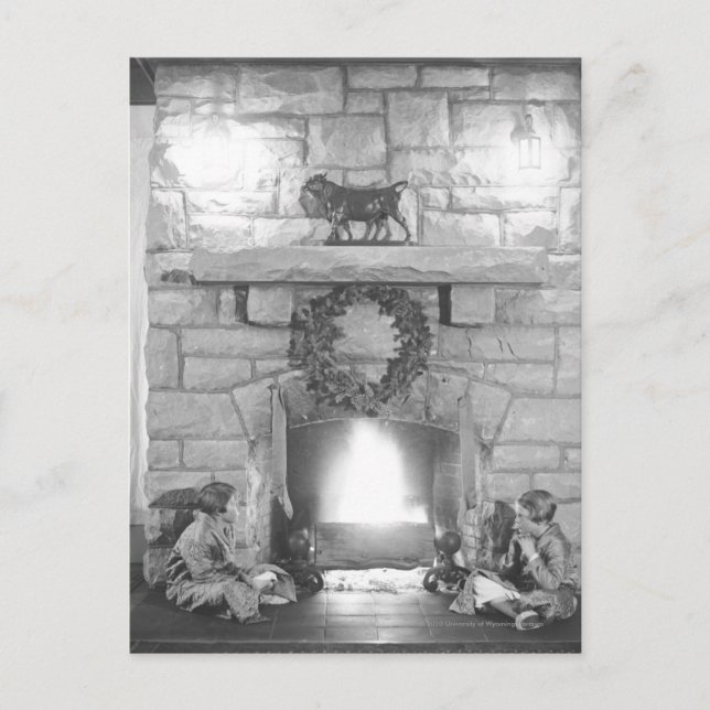 Two girls sitting by a fireplace at Christmas Holiday Postcard (Front)