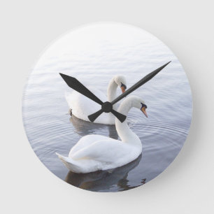 Two Swans Swimming on Tranquil Lake Round Clock