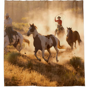 Two western cowboys riding horses, roping wild hor