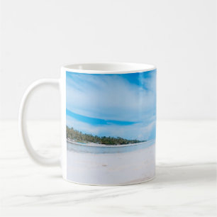 Two women lying on white sand facing beach under b coffee mug