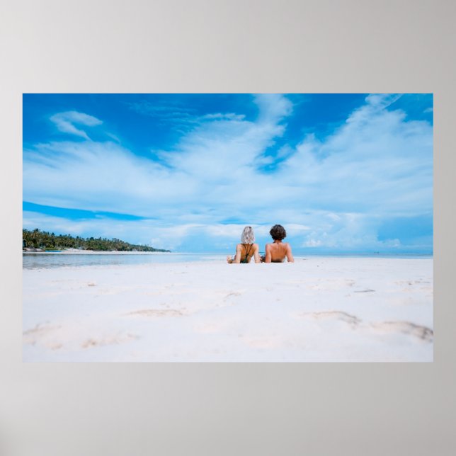 Two women lying on white sand facing beach under b poster (Front)