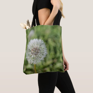 White dandelion flower on green grass tote bag
