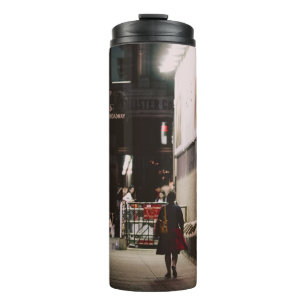 WOMAN IN BLACK AND RED DRESS WALKING BESIDE BROWN THERMAL TUMBLER