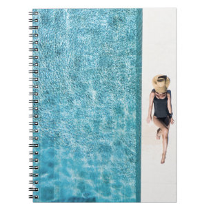 Woman in black bikini bottom and white sun hat sta notebook