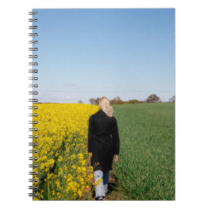 Woman in black coat standing on green grass field  notebook