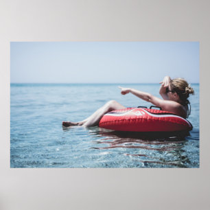 Woman on an inflatable float in the ocean pointing poster
