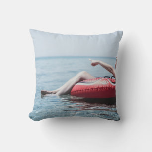 Woman on an inflatable float in the ocean pointing throw pillow