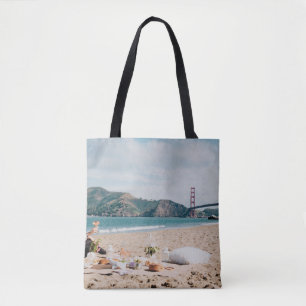 Woman sitting near seashore while looking at Golde Tote Bag