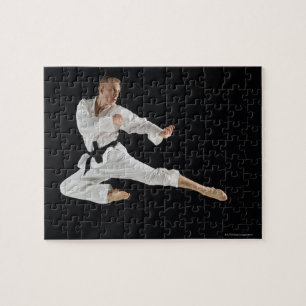 Young man performing karate kick on black jigsaw puzzle