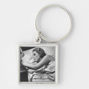 Young woman lying on bed turning off lamp on keychain