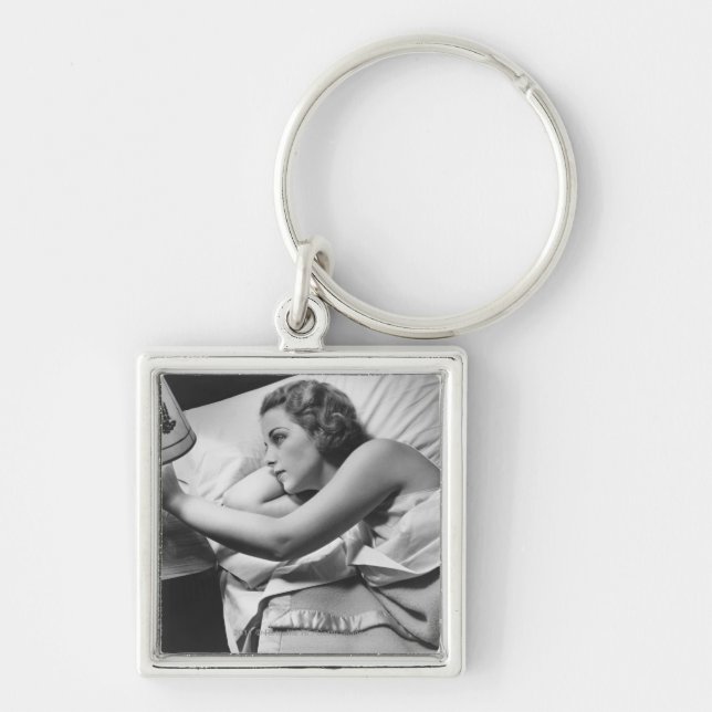 Young woman lying on bed turning off lamp on keychain (Front)