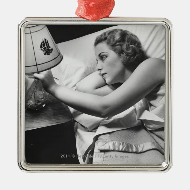 Young woman lying on bed turning off lamp on metal ornament (Front)
