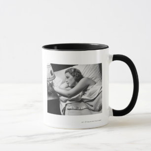 Young woman lying on bed turning off lamp on mug